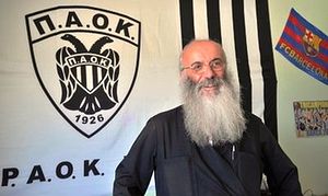 In this Wednesday, June 8 , 2009 photo, Orthodox priest Father Christos Mitsios poses in front of a banner of Greek football club PAOK Thessaloniki, in Thessaloniki, Greece.