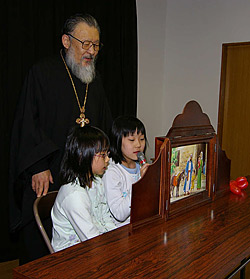 Rector of the church in Sapporo Archpriest Alexis Matsudaira is helping Alexandra Yamaguti and Rebecca Sato show “holy pictures”.