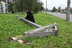 A Russian Orthodox priest crouching down by a felled cross in Arkhangelsk