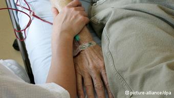 A woman holds the arm of an old man wishing to die in the hospital to support him 