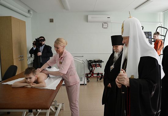 Святейший Патриарх и епископ Пантелеимон смотрят, как высококвалифицированный массажист работает с ребенком