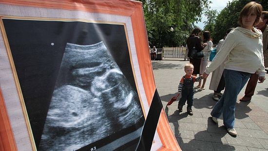 A pregnant woman and her child pass by a banner with an echography of a fetus during a rally against abortion in Moscow (AFP Photo / Alexey Sazonov)