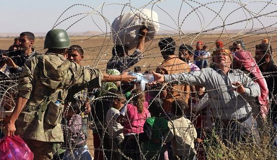 A Turkish soldier gives a bottle of water to a handicapped Syrian refugee waiting at the border in Suruc, Turkey, Sunday, Sept. 21, 2014. Photo by AP