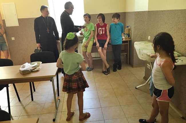 Refugee children at the LOGOS Center in Kyiv are drawn to Bishop Daniel, joined by the Very Rev. Mykola Ilnytsky, director of the LOGOS Center.