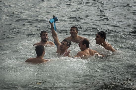 A man holds up the wooden cross after being the first to retrieve it, during an Epiphany ceremony to bless the water in Mytilene port on the northeastern Greek island of Lesbos, Wednesday, Jan. 6, 2016. Similar ceremonies to mark Epiphany Day were held across Greece at the sea, rivers, lakes and dams. An Orthodox priest throws a cross into the water and the swimmers race to retrieve it first. (Santi Palacios/Associated Press)