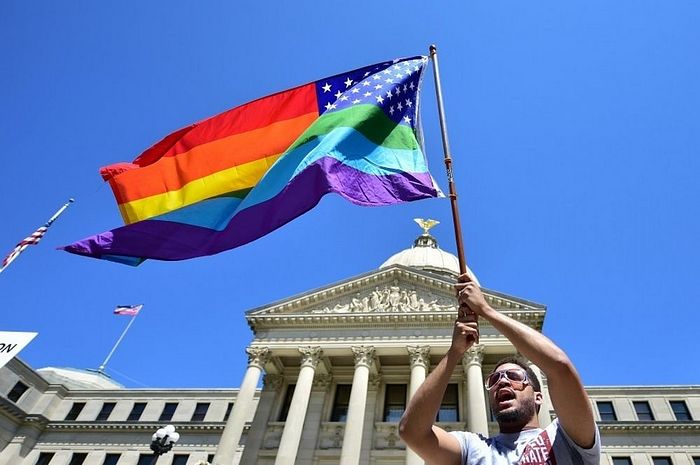 Meridian resident Nykolas Alford waves a rainbow-colored flag designed with the U.S. flag during a Human Rights Campaign protest of House Bill 1523 on the Mississippi State Capitol steps in Jackson, Miss., Tuesday, March 29, 2016. (Justin Sellers/The Clarion-Ledger via AP)