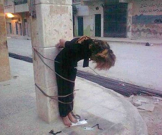 Женщина-христианка у столба. У ее ног надпись: «У того, кто не плюнет в эту женщину, нет чести». Фотография сделана в «освобожденном» Сирийской свободной армией районе Алеппо